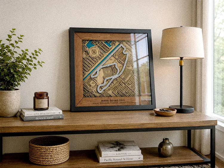 A framed art print of a Miami Beach Pool golf course map, styled on a wooden console table with a lamp, books, and a plant in a bright room.