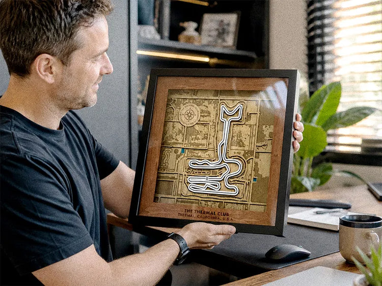 A man in a black t-shirt holds up a framed 3D papercartel map of the Thrasher Club in Los Angeles, California, in an office setting.